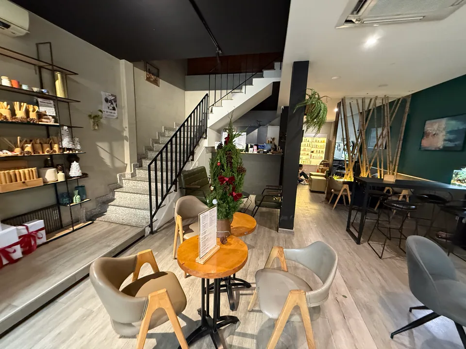 Cầu thang xám dẫn lên tầng spa, vách bê tông sơn xanh ô-liu và một dãy bàn cao với ghế bar gỗ.